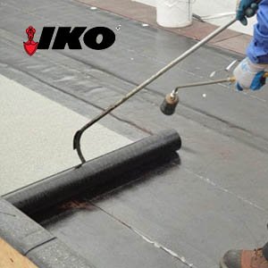 Working applying a torch down roof system with the IKO logo on the top left
